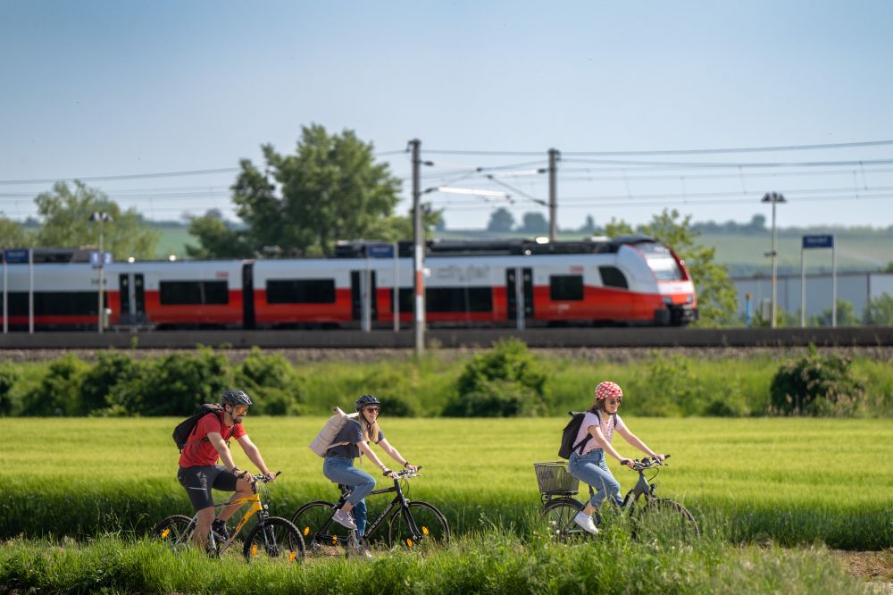 3 Menschen fahren Rad vor einem ÖBB Zug